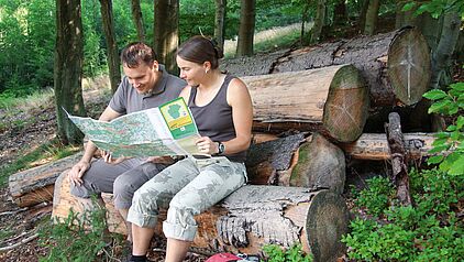 Zwei Wanderer mit Wanderkarte sitzend auf einem Baumstumpf